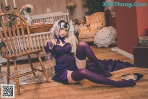 A woman in a purple dress sitting on a wooden chair.