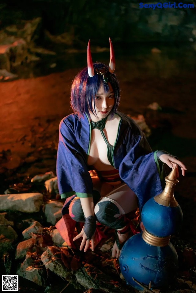 A woman in a blue kimono crouching down next to a blue vase.