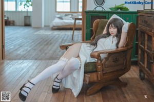 A woman in a white dress sitting on a wooden chair.