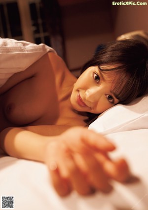 A naked asian woman sitting on a bed.