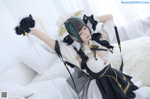 A woman in a maid outfit sitting on a bed.