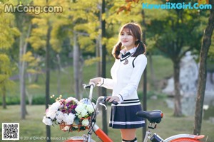 A woman in a school uniform holding a camera and a bicycle.