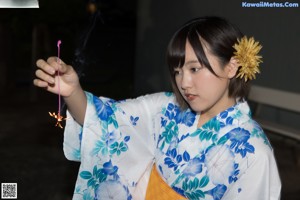 A woman in a blue and white kimono holding a flower.