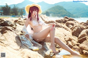 A woman in a white bikini and a straw hat on the beach.