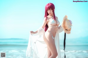 A woman in a bikini and a straw hat on the beach.