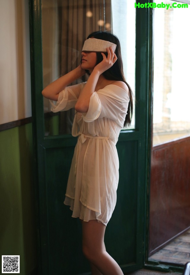 A woman in a white dress with a blindfold on her face.