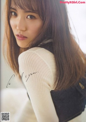 A woman with long brown hair wearing a beige jacket.