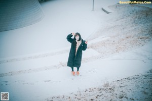 A woman leaning against a tree in the snow.