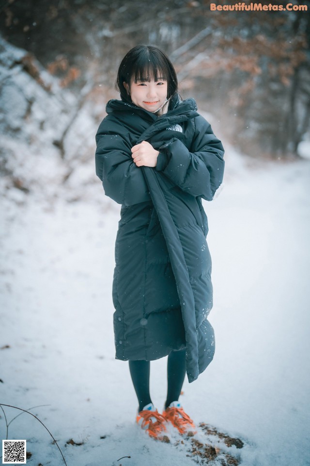 A young girl standing in the snow wearing a black coat.