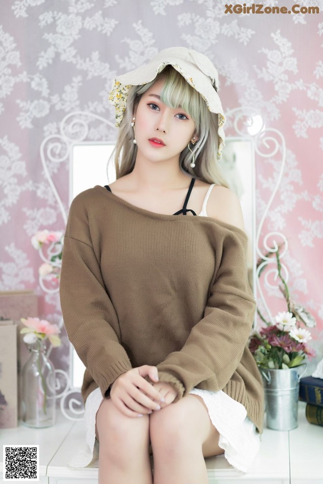 A woman sitting on top of a white dresser wearing a brown sweater.