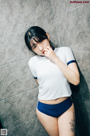 A woman in a white shirt and blue panties standing in a bathroom.
