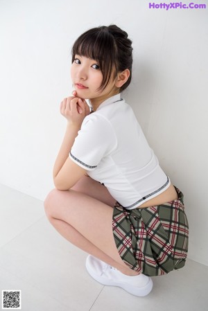 A woman in a white shirt and plaid skirt standing in front of a white background.