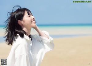 A woman in a white shirt dress walking on the beach.