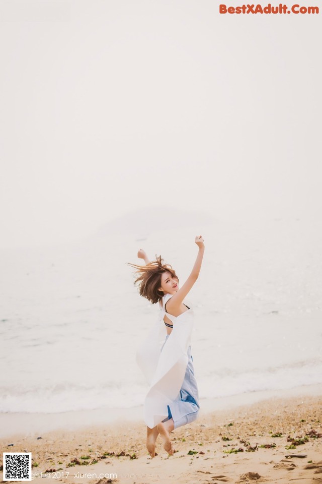 A woman in a white dress is jumping in the air on the beach.