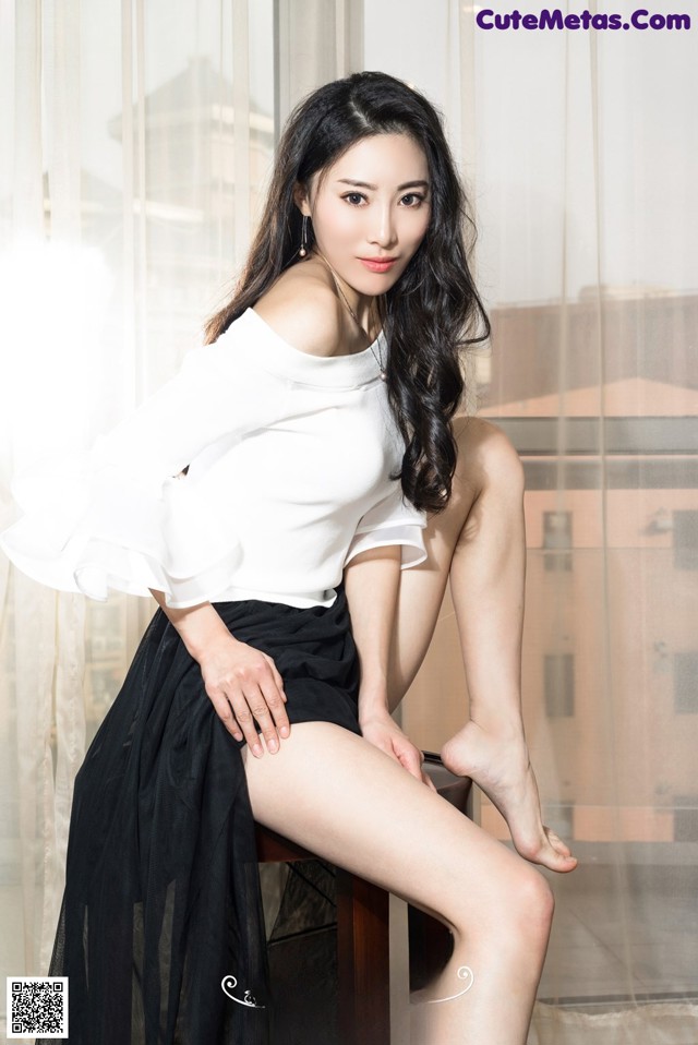 A woman sitting on top of a wooden chair next to a window.