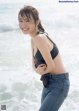 A woman in a black bikini standing on a beach.