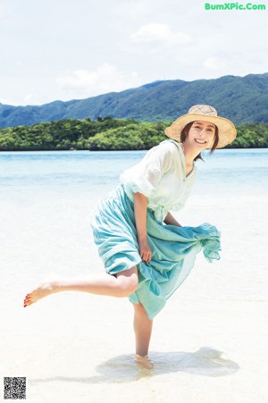 A woman in a blue dress and a straw hat on a beach.