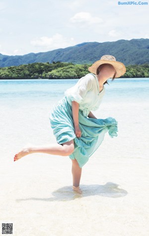 A woman in a blue dress and a straw hat on a beach.