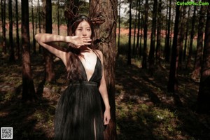 A woman in a black dress standing in the woods.