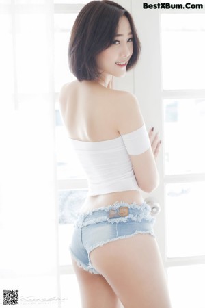 A woman in a white top and denim shorts holding a broom.