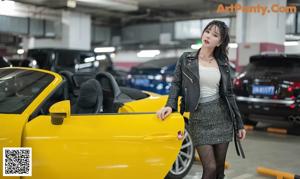 A woman in a black leather jacket sitting in a yellow car.