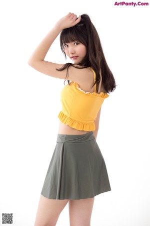 A woman in a yellow top and gray skirt posing for a picture.