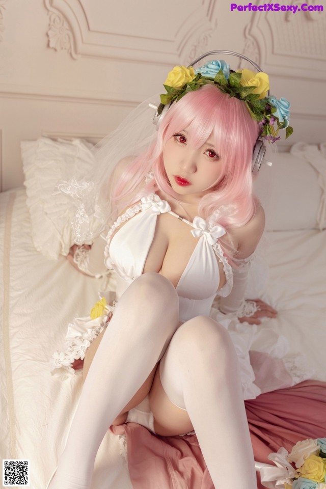 A woman in a white dress sitting on a bed.
